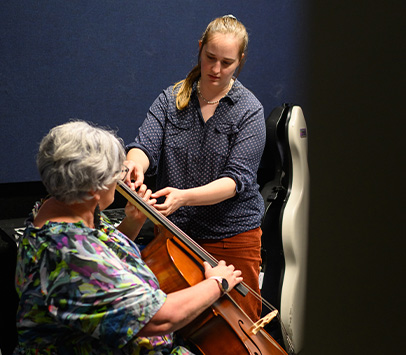 Woman teaches another woman how to play the cello during her individual lessons.